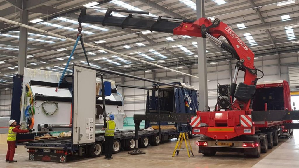 Red crane lifting large machinery in a warehouse