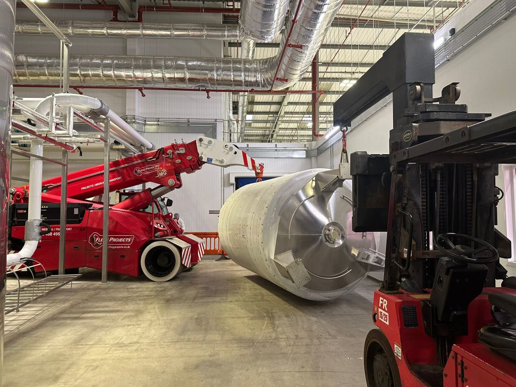 large silver holding tank moved in a factory with machinery